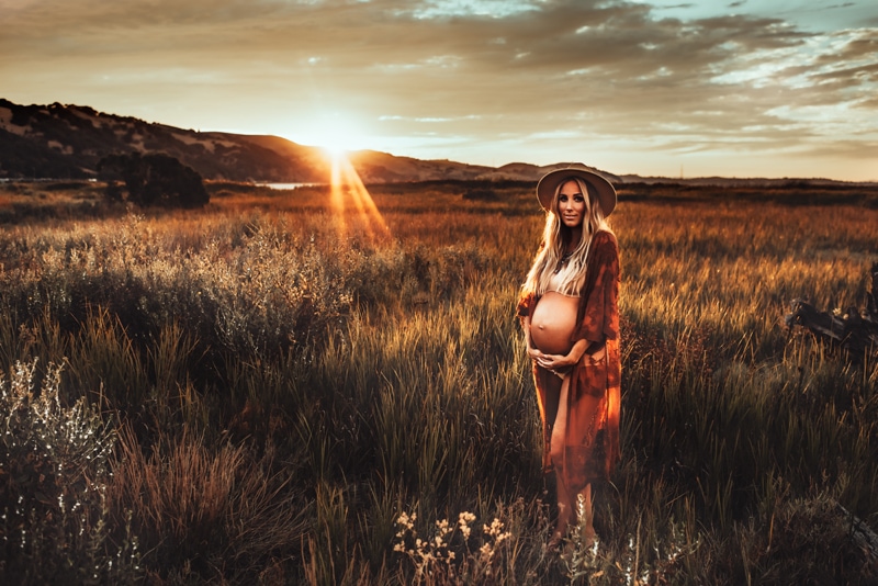 Bay Area Maternity Photography, wide angle of woman in field with sunset behind her